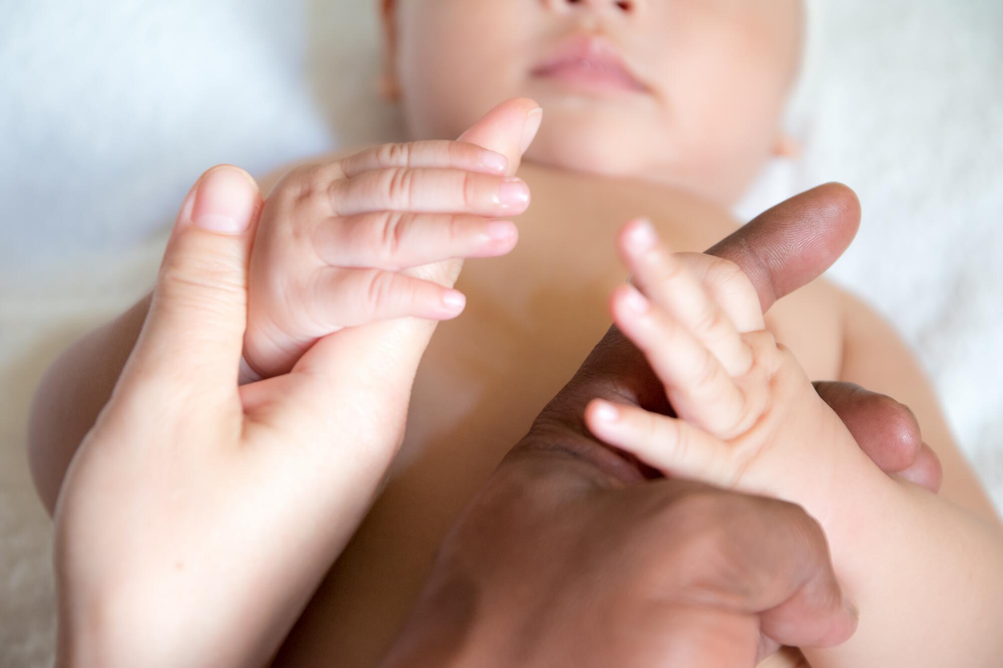 Baby som holder rundt tomlene til foreldrene.